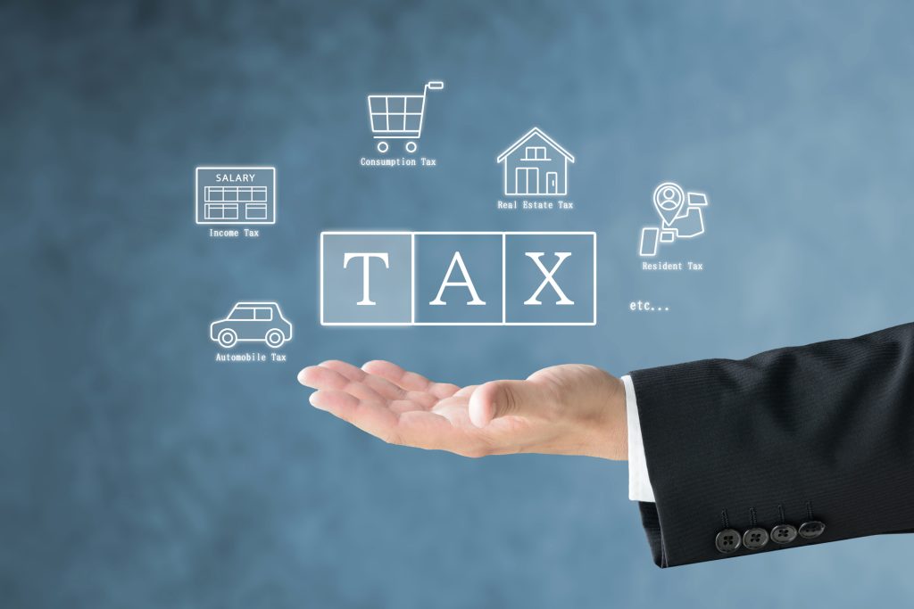 A man's hand in a suit holding up various tax icons and the word TAX